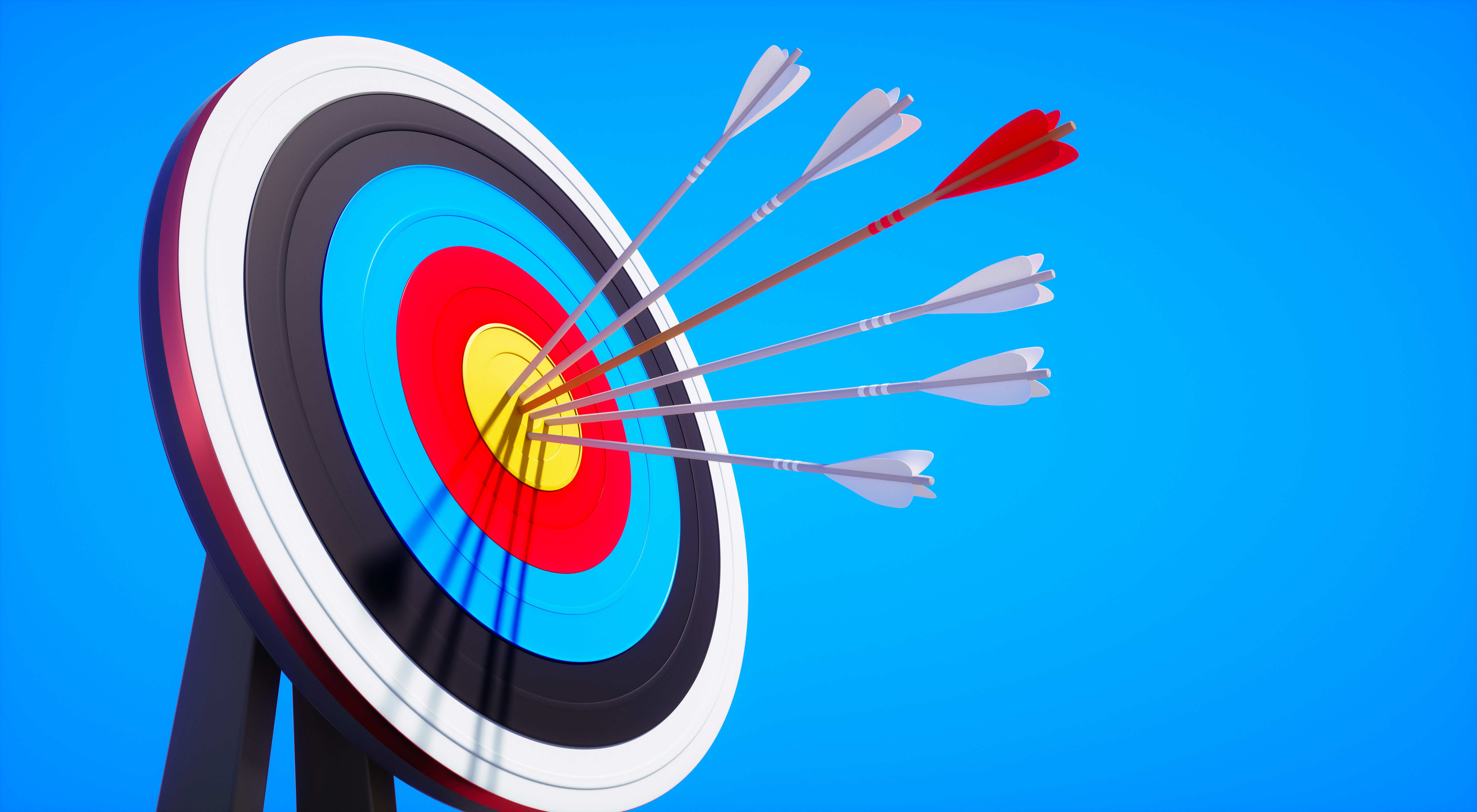 An archery target with arrows in the bullseye, against a blue sky