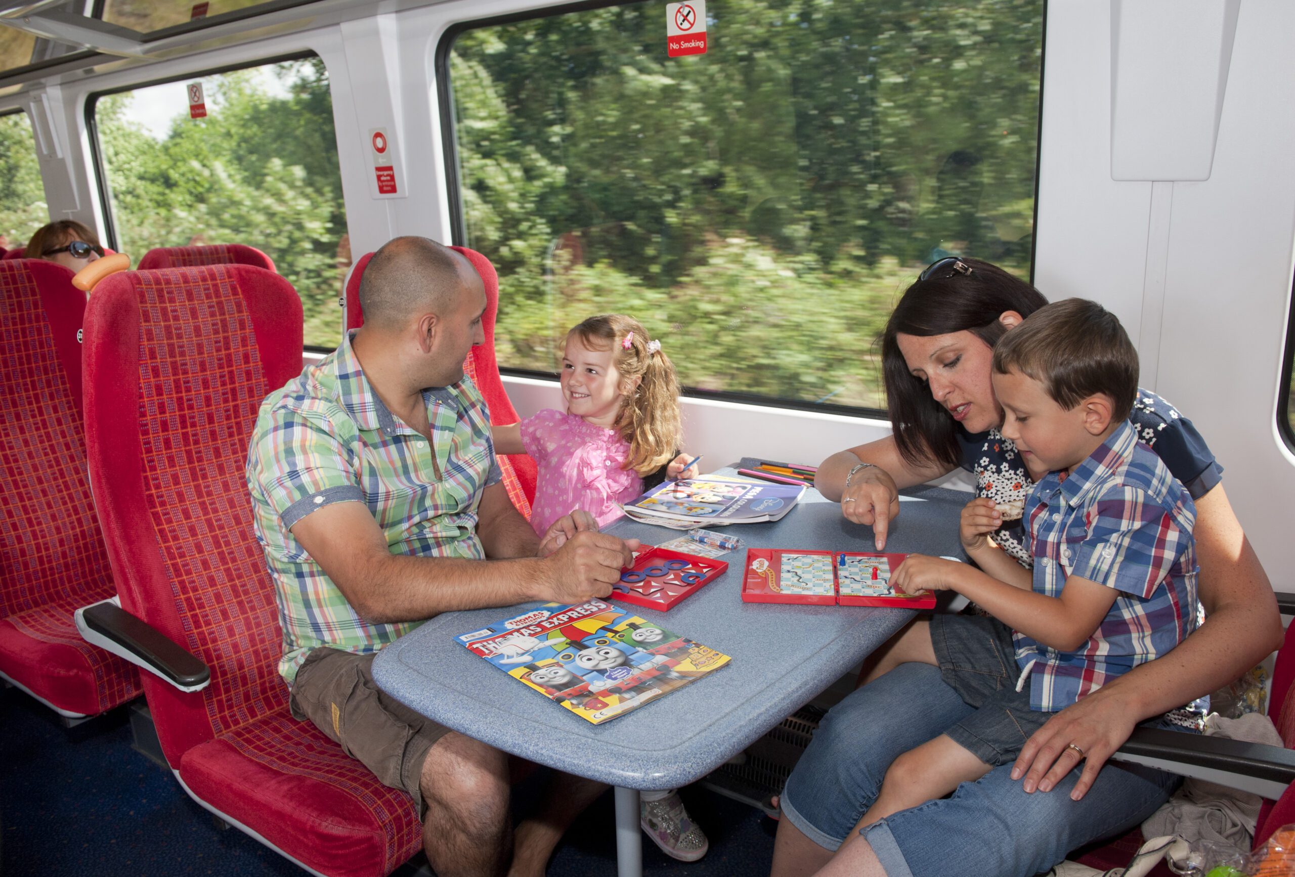 A family sitting at a table on a train playing games and colouring in.