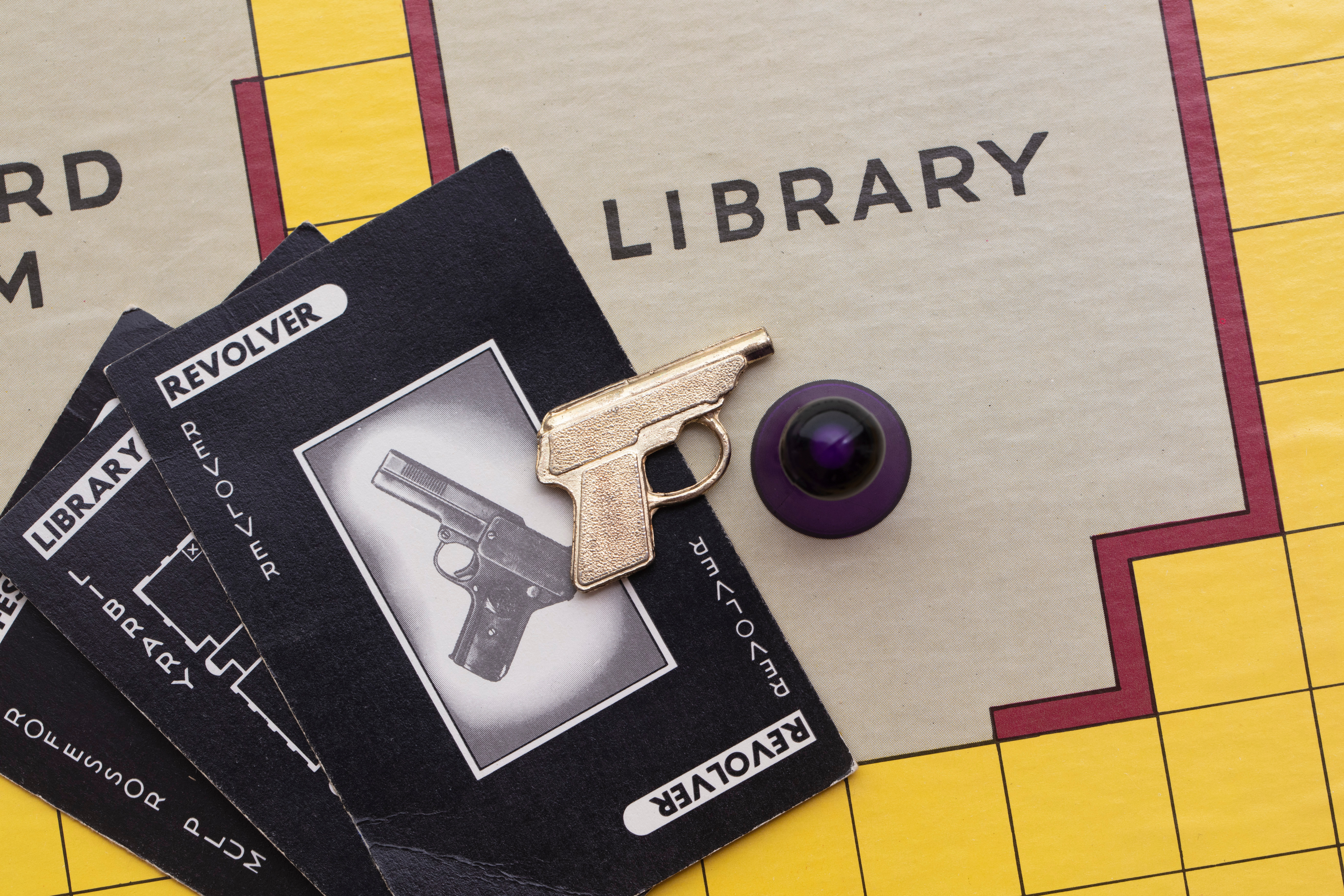 Part of a Cluedo board with a counter, mini revolver and Cluedo cards
