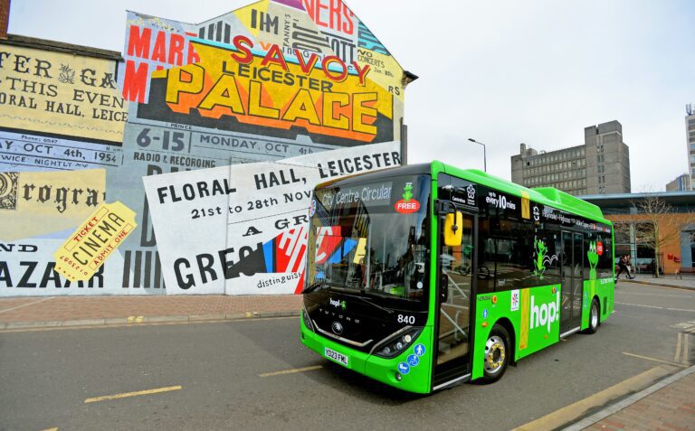 A single decker bus in Leicester driving past the gable end of a building which is covered in vibrant street art.